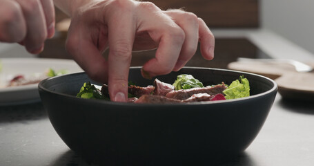 Man hand add ribeye steak slices in salad in black bowl