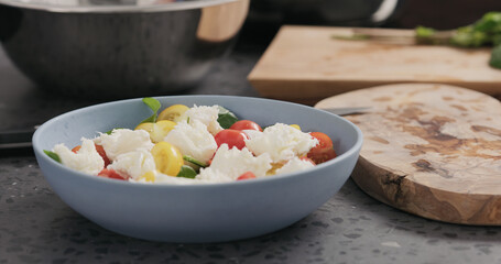 Closeup making salad with spinach, tomatoes and mozzarella in ablue bowl on concrete countertop