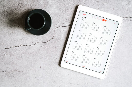 a tablet with an open calendar for 2021 year and a cup of coffee on a gray concrete background