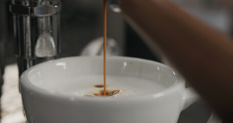 coffee extraction from professional coffee machine into cup with steamed milk