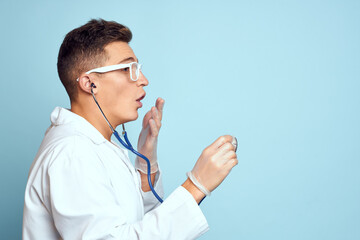 A medical worker in a dressing gown and glasses holds a stethoscope in his hands on a blue background cropped view