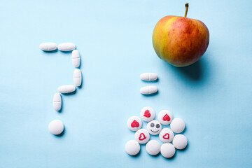 question mark made of white pills, a ripe apple and a bunch of white pills with a face and a heart