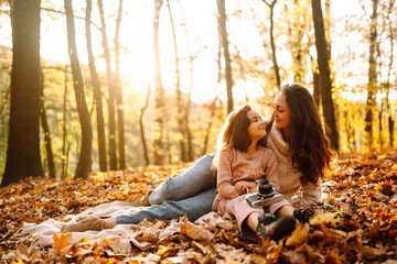 Young Mother and daughter  having fun together in the autumn forest. Mom and child embrace at sunset. Rest on autumn park.