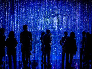 Silhouettes of people standing in front of blue led light string