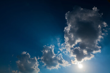 Naklejka na ściany i meble Sun and big clouds in the dark blue sky (backlight)