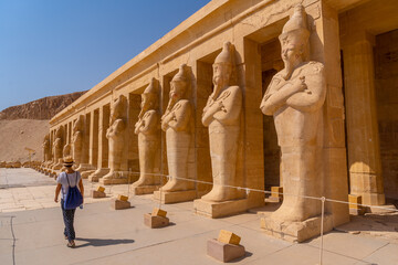 Fototapeta premium A young woman with pharaoh sculptures entering Hatshepsut's Funerary Temple in Luxor. Egypt