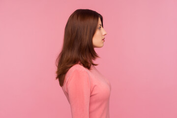 Profile portrait beautiful self confident woman in pink sweater looking at distance with serious expression. Indoor studio shot isolated on pink background