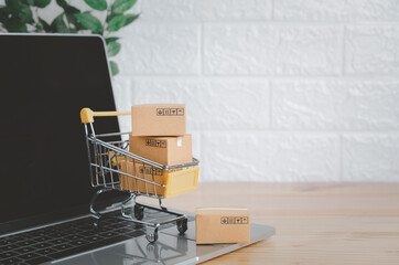 Online shopping and delivery service concept.Brown paper boxs in a shopping cart with laptop on wood table in office background.Easy shopping with finger tips for consumers.
