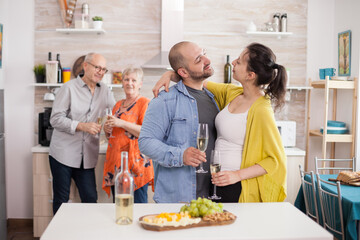 Couple looking at each other in kitchen during family brunch. Man holding glass of wine. Appetizer with various cheese.