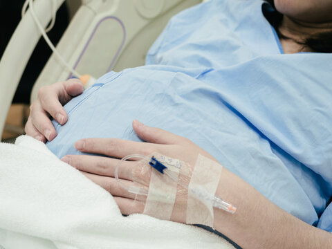 Pregnant Woman patient is waiting to deliver baby with drip receiving a saline solution on bed  at hospital, selective focus. Health Care concept, insurance concept, mother concept