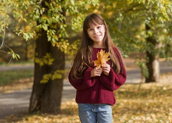 Foto op Plexiglas Aanbiddelijk meisje in glimlacht. Het kind houdt bladeren vast in het herfstpark. © Albert Ziganshin
