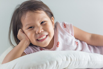 Portrait of cute happy asian little girl lying in bed with a big smile.