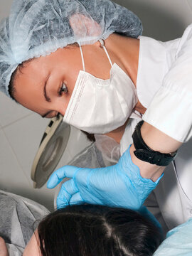 Dermatologist cosmetologist visit patient before beauty procedure or face lifting, beautiful woman doctor, dress with surgical cap and mask with surgical gloves observes the patient skin