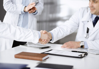 Unknown doctors are shaking their hands as agreement about patient's diagnosis, close-up. Medical help, insurance in health care, medicine concept