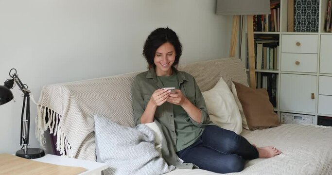 Woman resting on sofa in living room hold smartphone having pleasant chat with boyfriend informal communication remotely, smiles daydreams enjoy lazy weekend day use modern wireless technology concept
