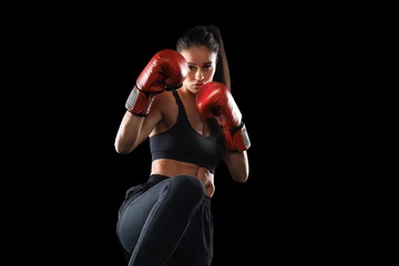 Tuinposter Kickboxing woman in activewear and red kickboxing gloves on black background performing a martial arts kick. Sport exercise, fitness workout. © ty