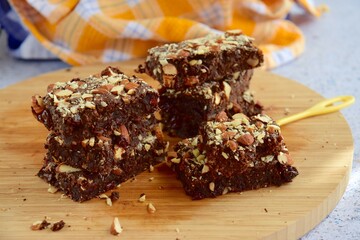 Fudge brownies dark chocolate cake topping with almond nuts on wooden board
