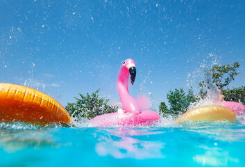 Funny action photo in the outdoor swimming pool with splashes of inflatable flamingo and doughnuts...