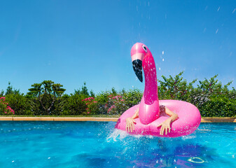 Funny photo of inflatable pink flamingo and child hands inside looking like very surprised bird in the pool © Sergey Novikov