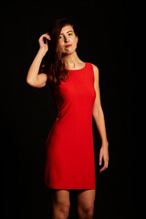 Young brunette Spanish woman dressed in sexy red dress, matching beaded earrings, and black shoes on black background,red
