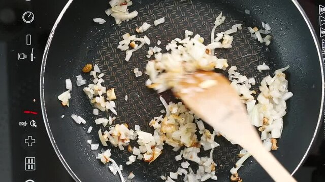 Overhead shot wooden spoon stirring sauted garlic and onion