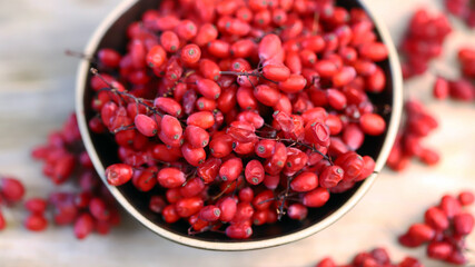 Berries and bunches of barberry in a bowl on a wooden surface. Barberry.