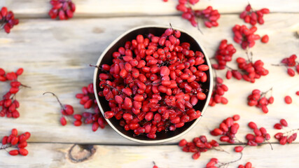 Berries and bunches of barberry in a bowl on a wooden surface. Barberry.