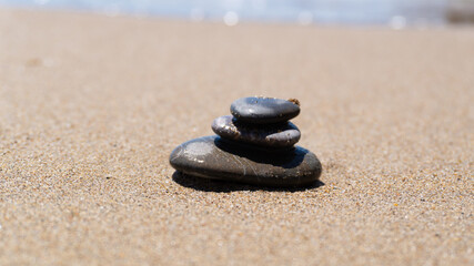 Fototapeta na wymiar Pyramid of sea pebbles on a sunny sand beach. Life balance and harmony concept. Stack of zen stones on pebble beach