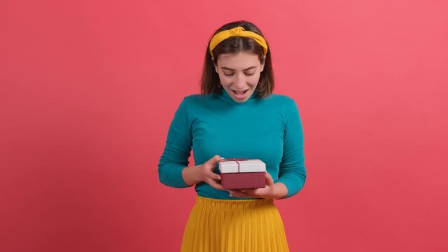 Portrait of a happy woman receiving a gift and opening it, isolated over red background.