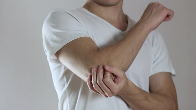 The man has a sore elbow, pain in the arm. Close up. Isolated on a gray background.