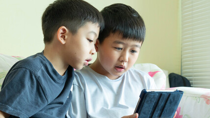 Two boys are playing the electronic tablet together at home.Children are enjoy watching the screen for fun.