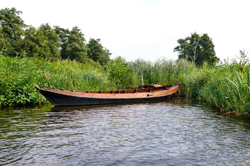 An abandoned wooden boat standing in the canal between the reeds.