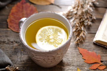 Hot cup of tea on a wooden background. White cup with tea and lemon on an autumn day. Autumn colorful leaves. Cozy concept.