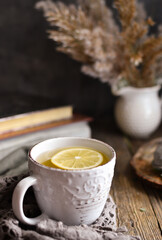 Hot cup of tea on a wooden background. White cup with tea and lemon on an autumn day. Autumn colorful leaves. Cozy concept.