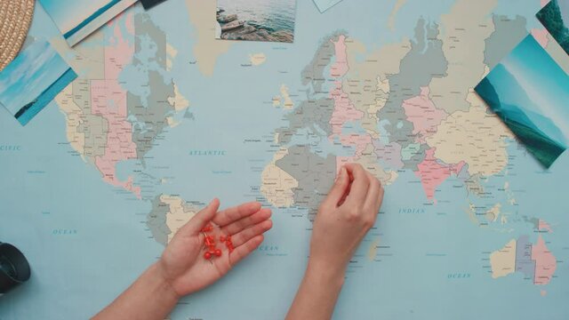 Horizontal top view flat lay footage of female hands holding thumbtacks and pushing them on world map to places of visiting