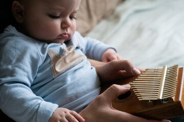 Parent spending time with family during coronavirus lockdown - father teaches little cute baby boy how to play tiny instrument calimba at home. Selective focus on instrument.