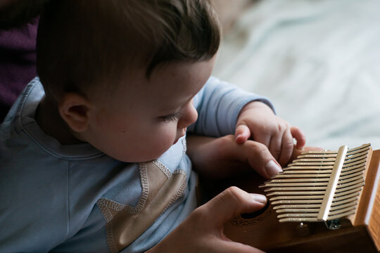 Parent spending time with family during coronavirus lockdown - father teaches little cute baby boy how to play tiny instrument calimba at home. Selective focus on instrument.