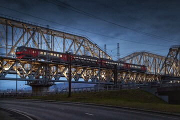Fototapeta na wymiar The Train moves at night on a lighted bridge over the river.