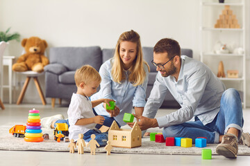 Mom, dad and baby playing at home with colored cubes sitting on the floor among colored toys.