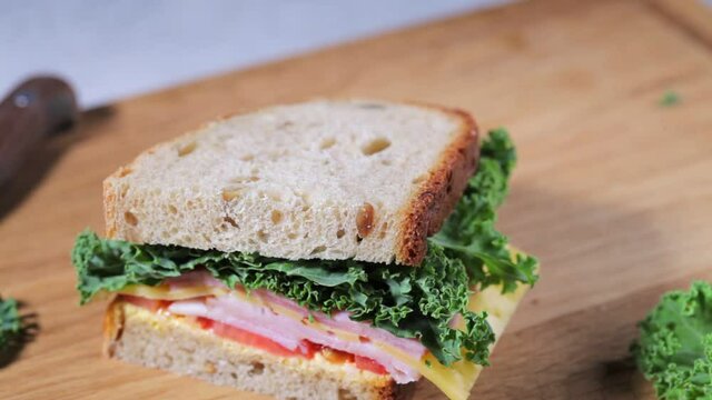 Eating sandwich with ham, cheese, vegetables and kale on a wooden board.