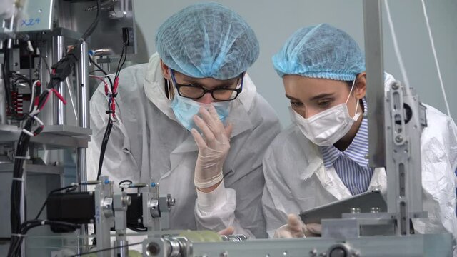 Group of engineer worker wearing ppe suite and face protective medical mask , glove useing digital tablet analyze  operation and check quality of mask manufacturing machine at lab in industry factory