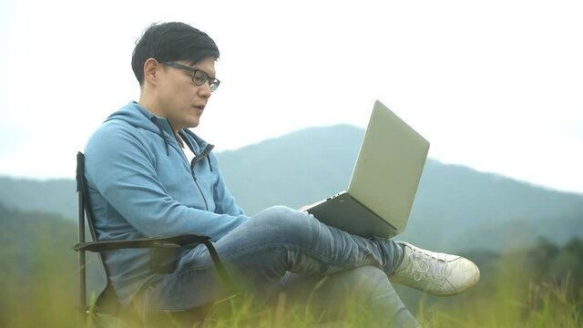 Tourist young man using laptop computer while enjoying sunset in mountains. Freelancer male working on netbook during vacation holidays in autumn. Distant work and travel, freelance as lifestyle