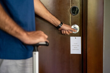 Tourist man opening disinfected hotel room. A sign hanging on the handle saying the room has been sanitized. New Normal, travel under Covid-19 pandemic, vacation and holiday concept