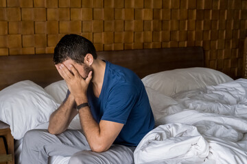 Stressed, depressed or grieving man sitting on bed covering face with hands and crying. Worried and frustrated male suffering depression or life crisis feeling desperate and helpless