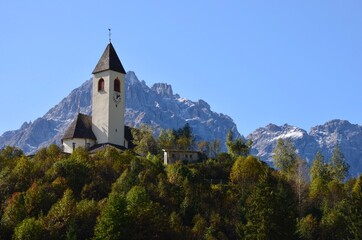 Fototapeta na wymiar Dolomites mountains near the village of Innichen in South Tirol (Alto Adige), Italy, a traditional church on a forested hill in front, colorful autumn landscape, blue sky background, a sunny day