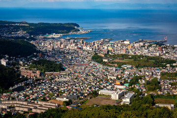 Fototapeta na wymiar 小樽山の展望台から見た、小樽の市街地とその奥にある石狩湾、雲の浮かぶ青空