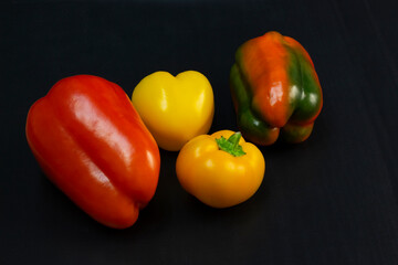 Red, green, and yellow bell peppers on black background. Four sweet peppers in different colors on stone table, vegetable ingredient, healthy food..