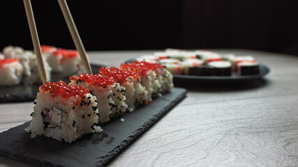 Female hand takes food with chopsticks.Sushi rolls japanese food rotated over black background. California Sushi roll with tuna, vegetables, flying fish roe and caviar close up, rotation. Japan