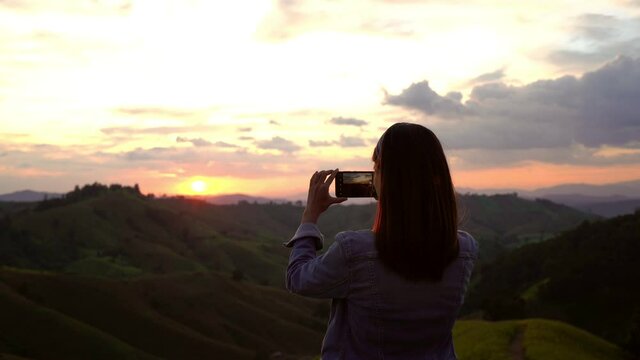 Young woman traveler taking a beautiful sunset over the mountains, Travel lifestyle concept