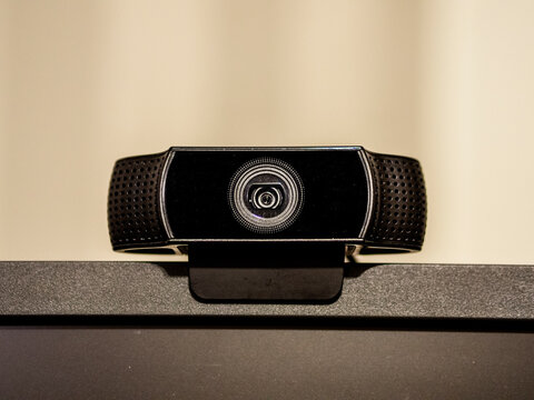 A black generic web camera on top of a screen. With a beige background.